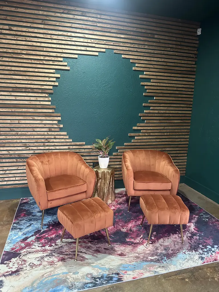 Two velvet lounge chairs on a marbled rug in front of a wood slat wall