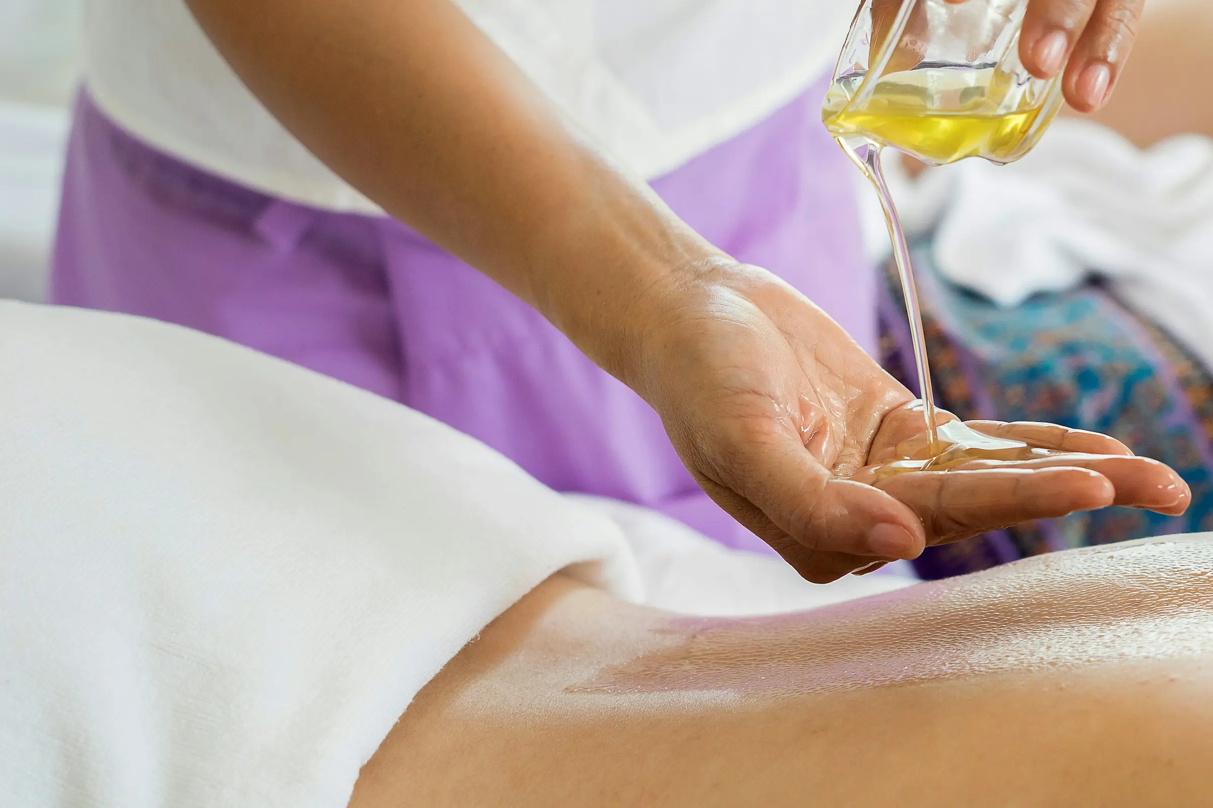 A therapist pouring massage oil into their palm above a client's back